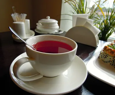 Изящная чашка чая в окружении ягод вишни. Вишневый чай стоит на плетеном  круглом подносе на фоне цветов. Солнечные лучи освещают чайную пару.  Stock-Foto | Adobe Stock